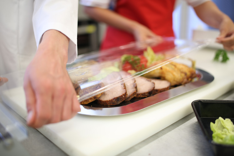 Frisch angerichtete Fleischplatte Mitarbeiterin richtet eine Platte mit Braten und Beilagen für den Partyservice an